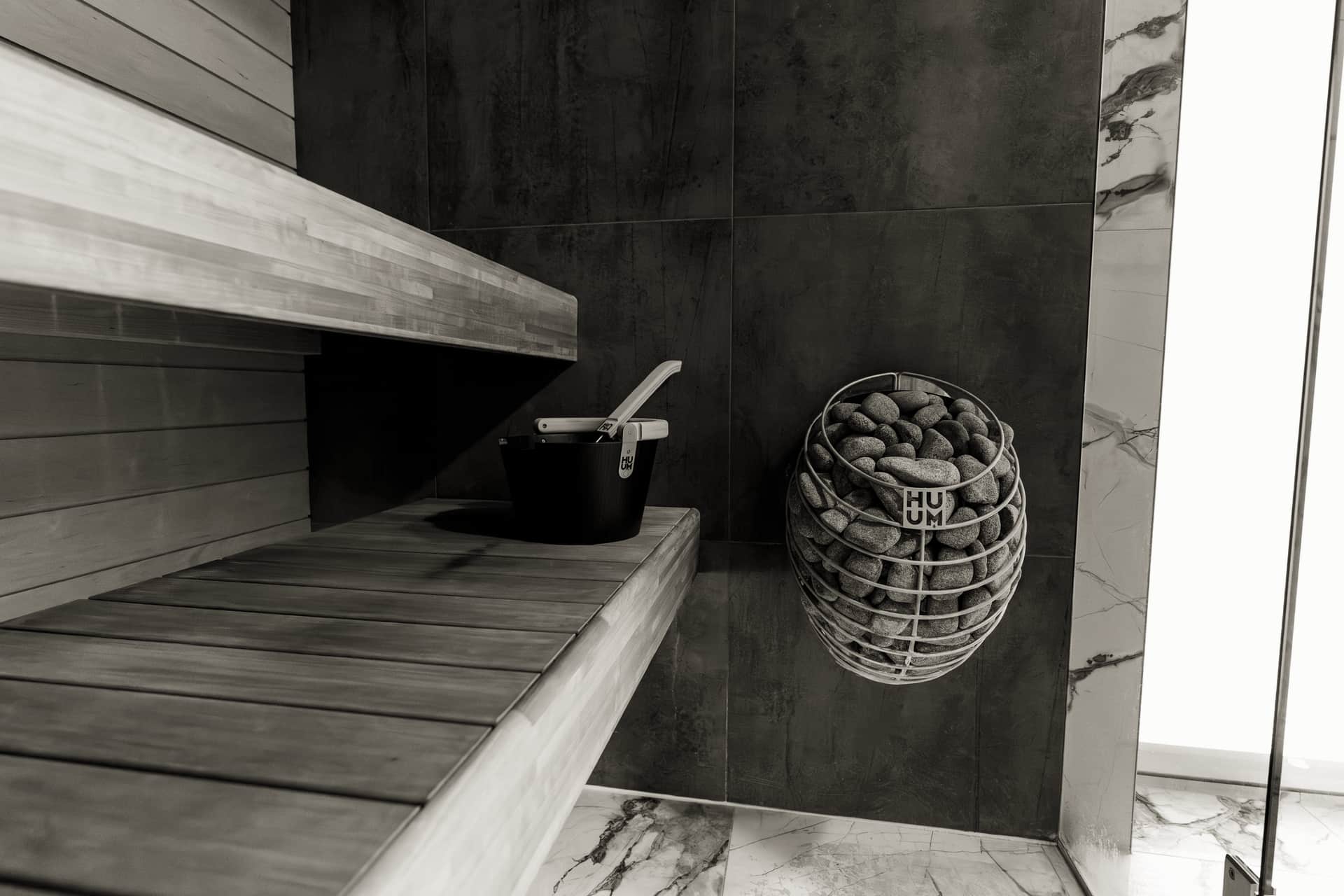 Wooden sauna bucket and ladle beside hot stones in a sauna interior